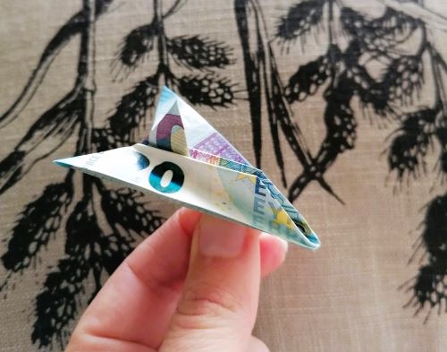 A hand holding an origami airplane made from Euro bills
