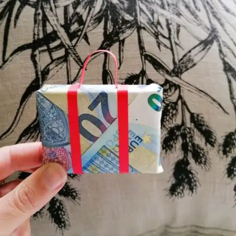 A hand holding an origami suitcase made from euro bills