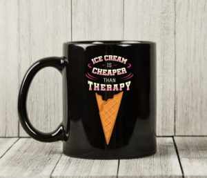 A black coffee mug with the funnt test "ice cream is cheaper than therapy"